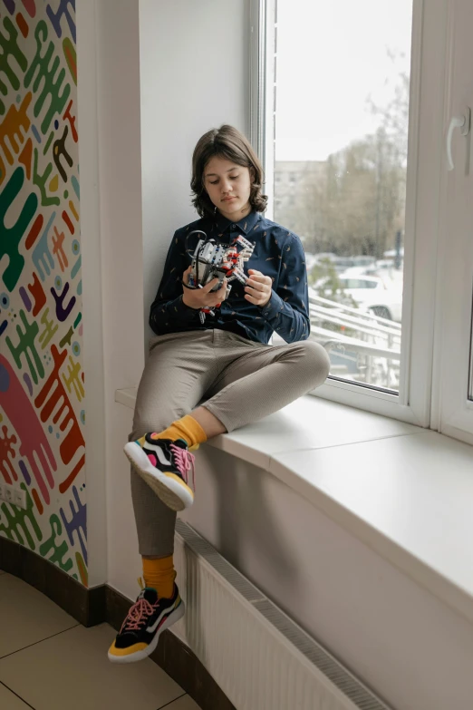 a girl sitting on the ledge with a camera looking through the window