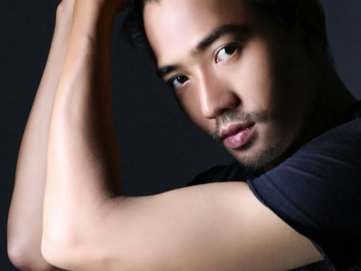 an asian man is standing and looking up with arms behind his head