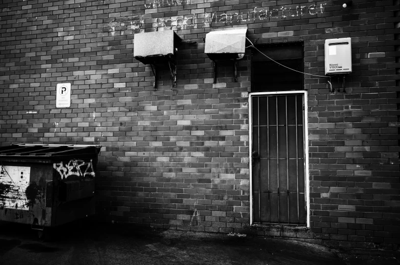 a black and white image of a brick building with two trash cans on the outside