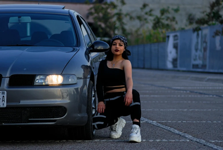 a woman sitting next to a car on the side of a street