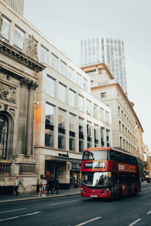 a red double decker bus driving down a street next to tall buildings