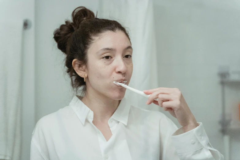 the woman in the white shirt is brushing her teeth