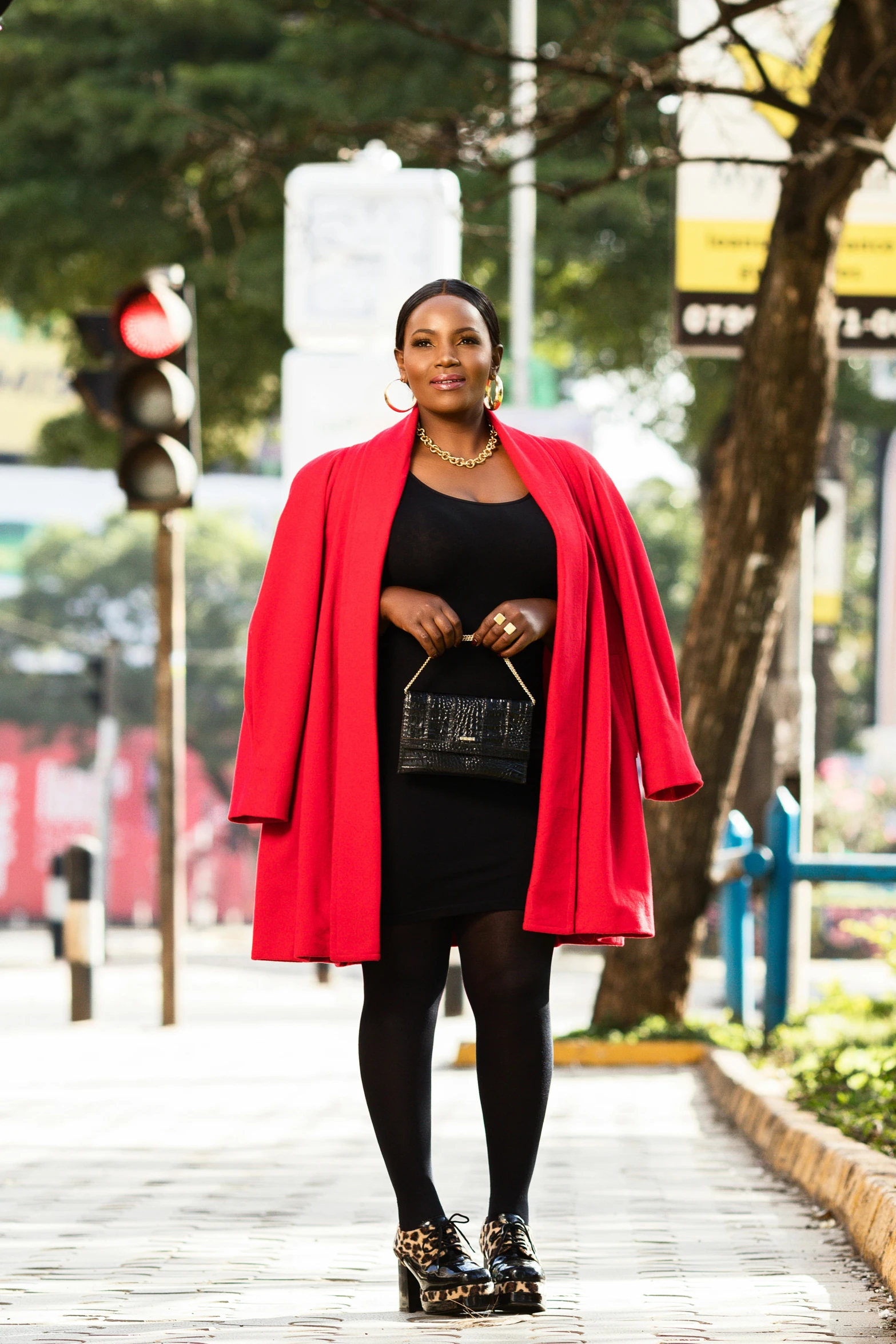 a woman is standing on the side walk and she has a red jacket over her shoulders