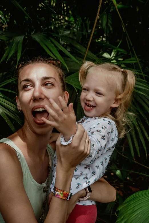 a young woman holding up a child who is standing in front of plants