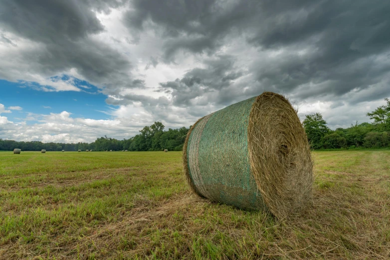 a field with hay bales under stormy clouds