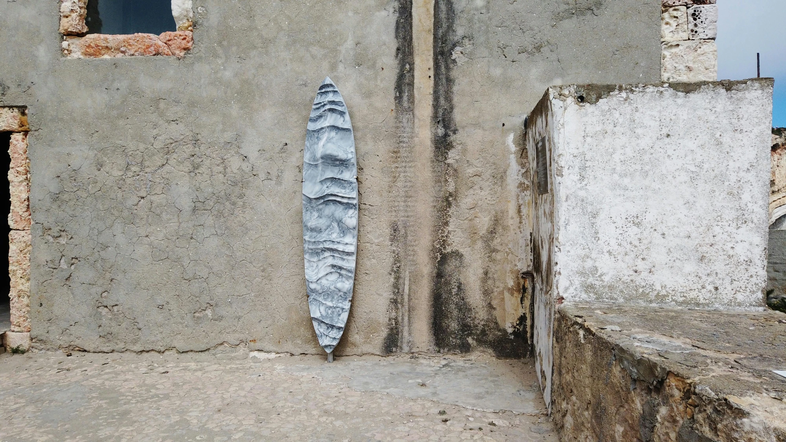 a broken surfboard leans against the stone wall of a cement building