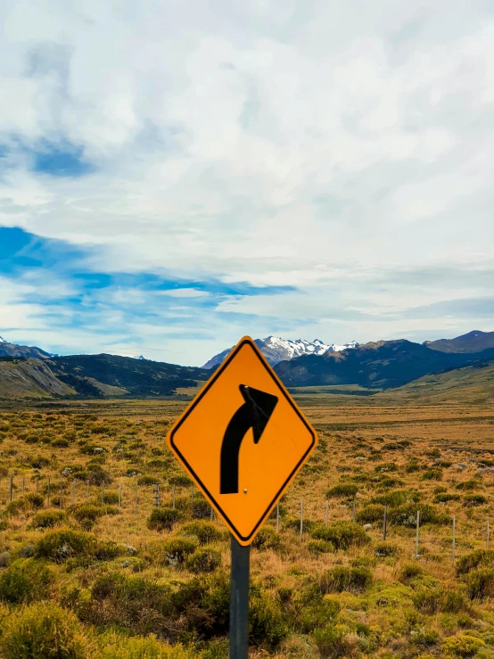 a sign in the middle of an open field with mountains in the background