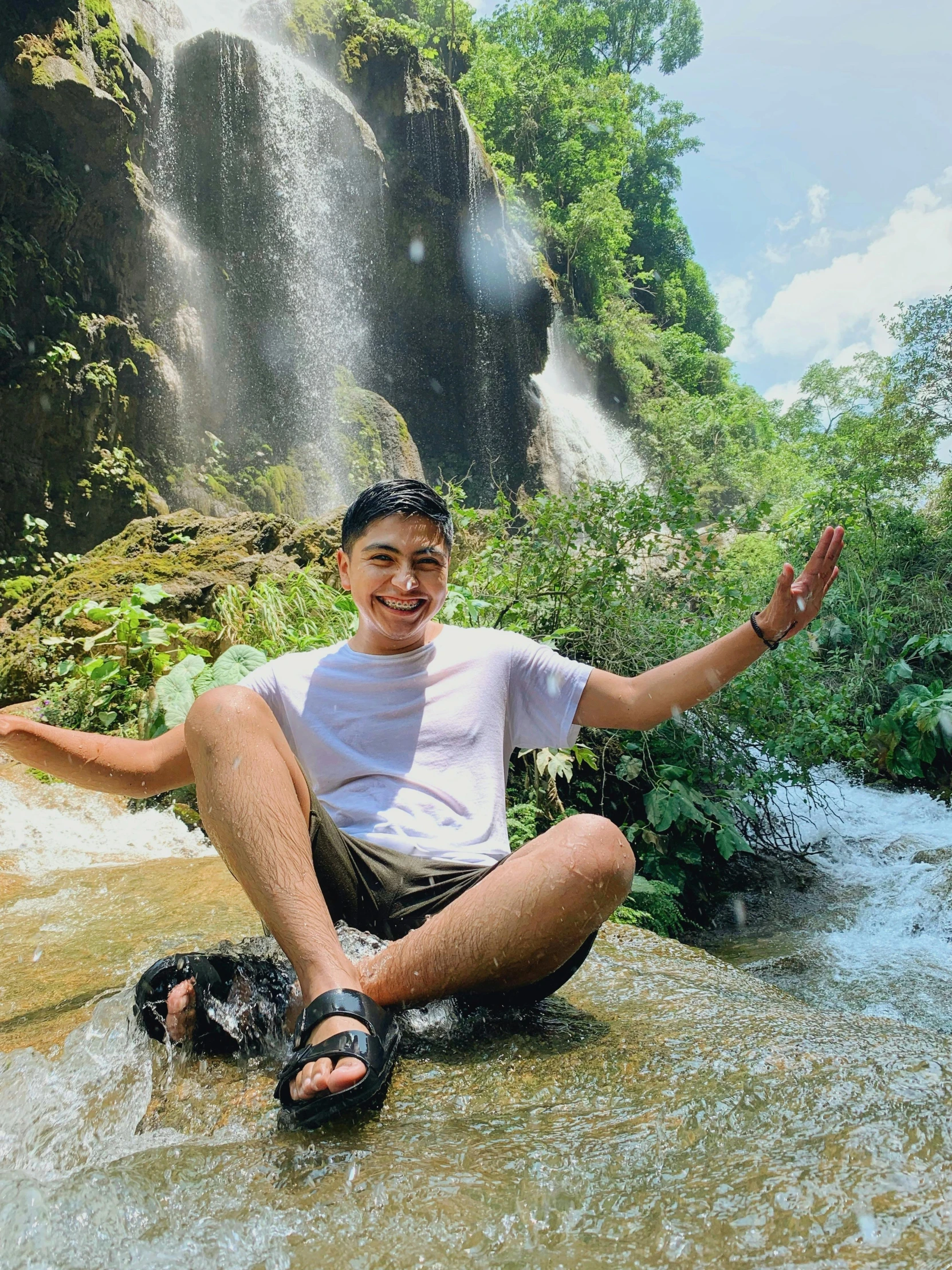 a man poses for the camera in front of an waterfall