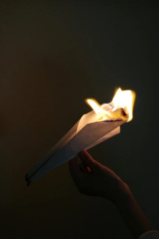 a person's hand is holding out a paper airplane that has fire on it
