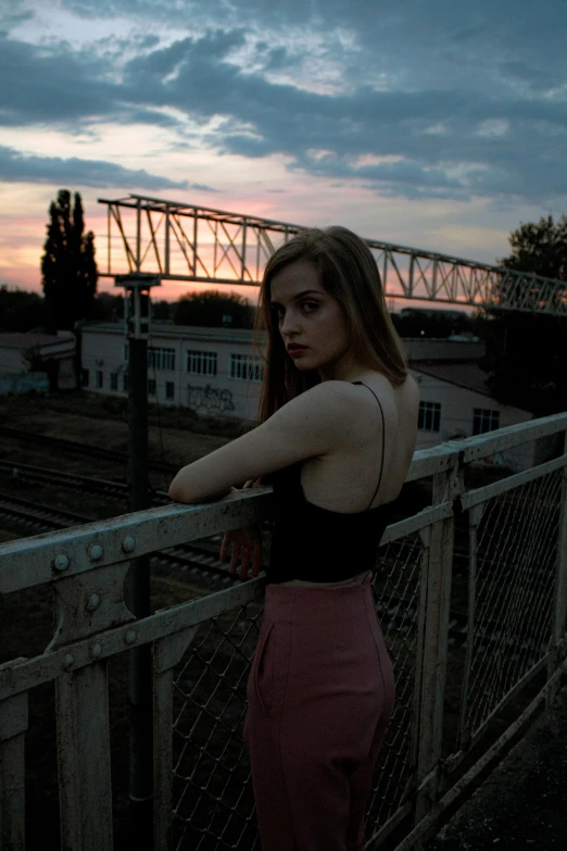 a woman leaning against a railing with the sunset in the background