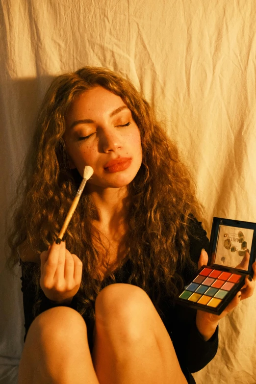 a woman is holding a small makeup palette and a brush