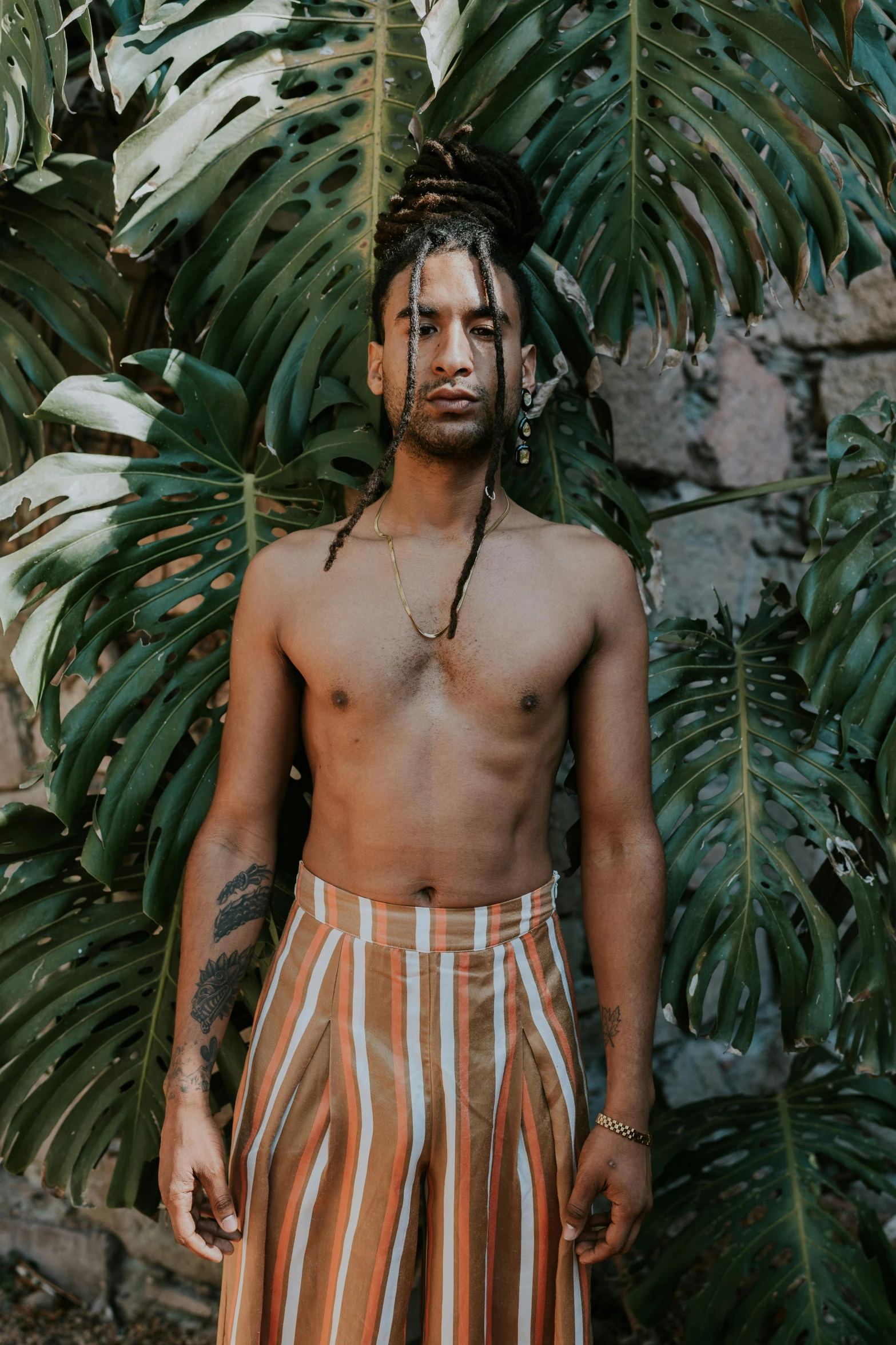 a man with long hair standing by a tree and some plants