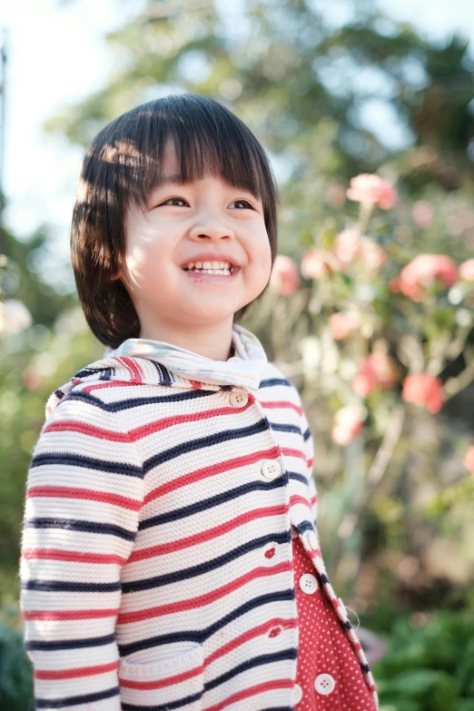 smiling girl in front of roses with a white shirt and a red striped cardigan