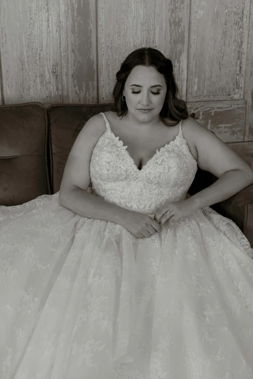 a plus size bride sits on a sofa wearing an off shoulder gown