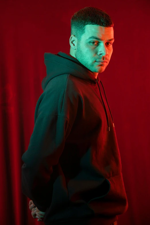 a young man wearing a black hoodie standing in front of a red curtain