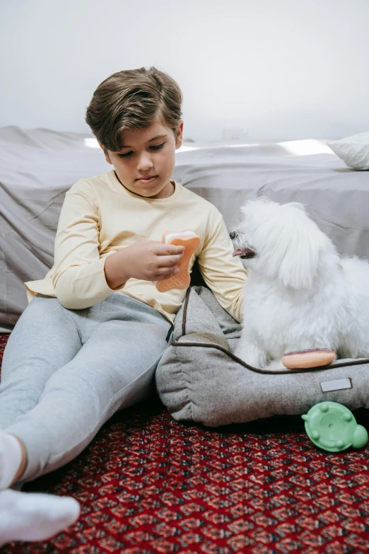 a boy with a small white dog sitting on a floor