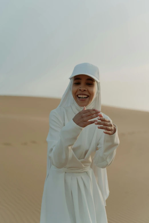 a woman dressed in white smiling and standing in a desert