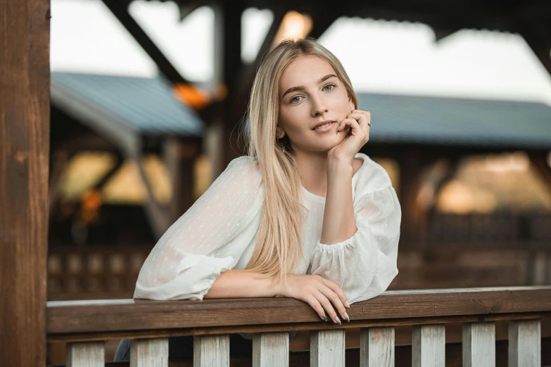 a woman wearing white leans on the wooden hand rail