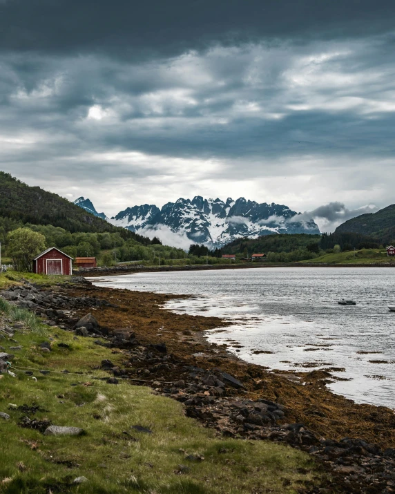 a small cabin sits near the water's edge with mountains in the distance