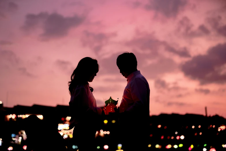 a man and woman standing close together, in front of the evening sky