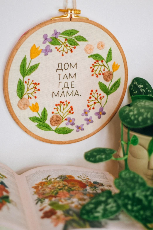 embroidered hoop hanging from wall with potted plant and book