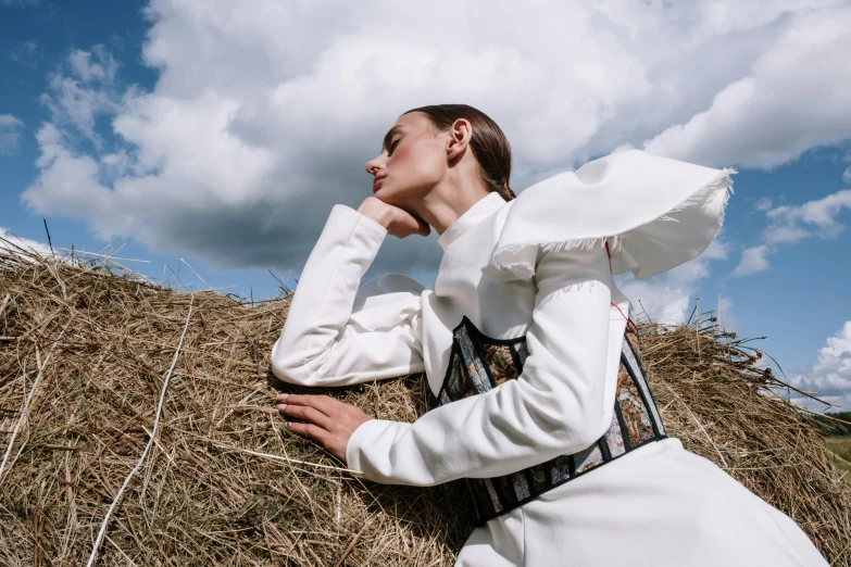 woman in a white dress leans over hay