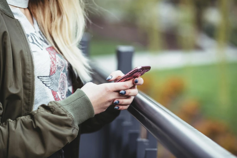 a girl looking at her phone while leaning against the fence