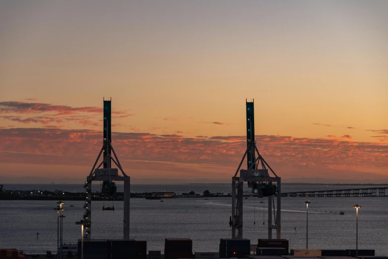 the sun is setting over the ocean with some large cranes near by