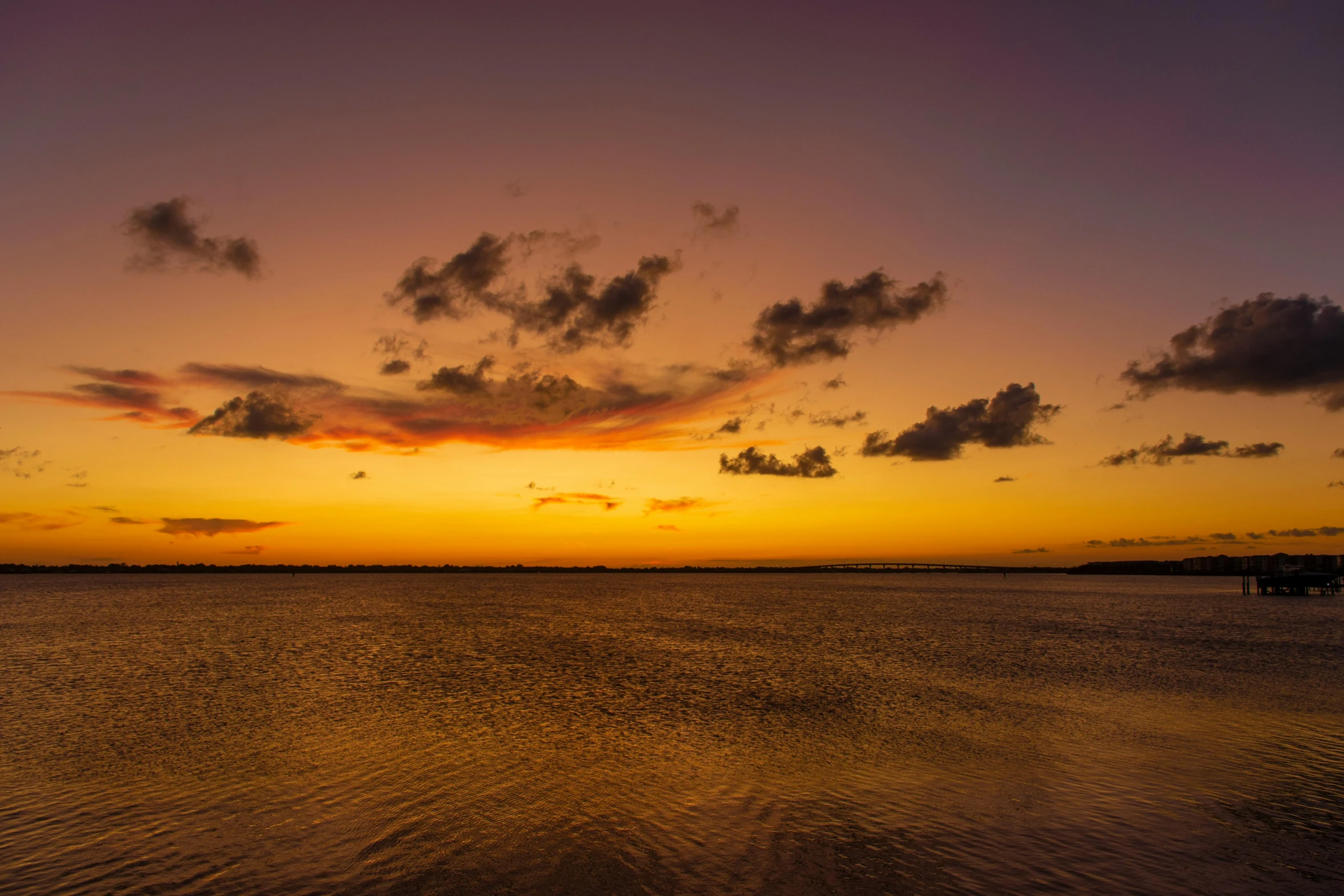 the sun rising over water with a pier in the background