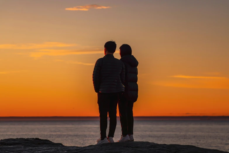 a couple standing on top of a rock next to the ocean