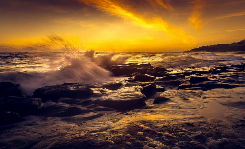 a sunset over a rocky beach with waves crashing into the shore