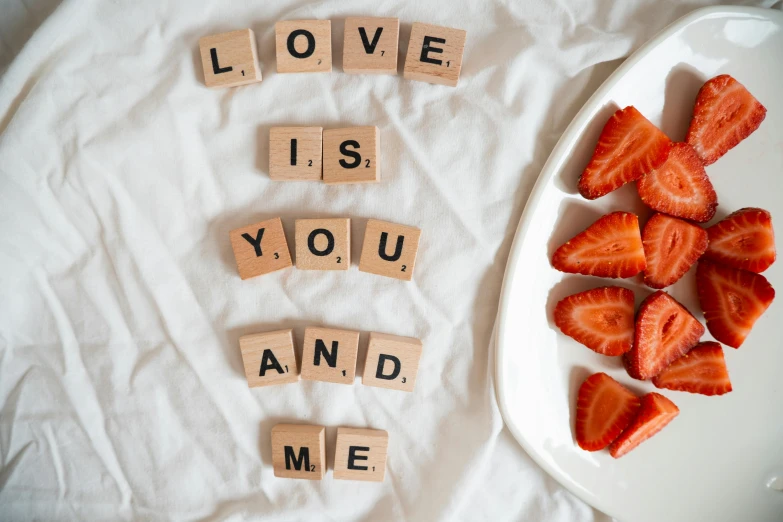 a plate with slices of strawberries sitting in it next to small scrabbles that spell out love