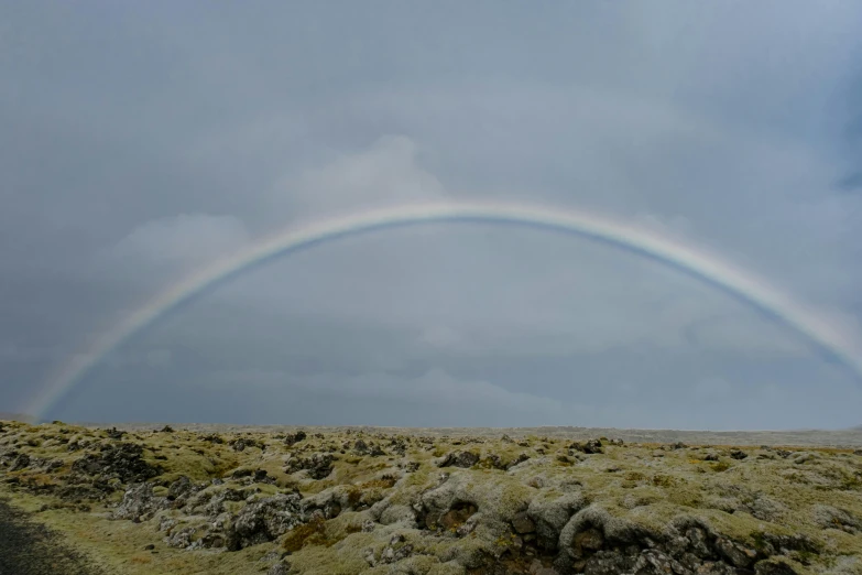 a rainbow appears over a field with dirt and grass