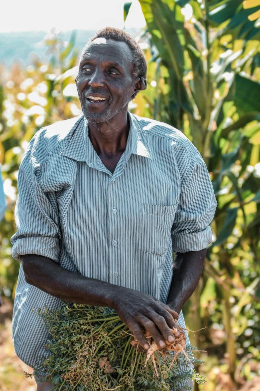 an older black man smiles as he stands with a grass plant in his hands