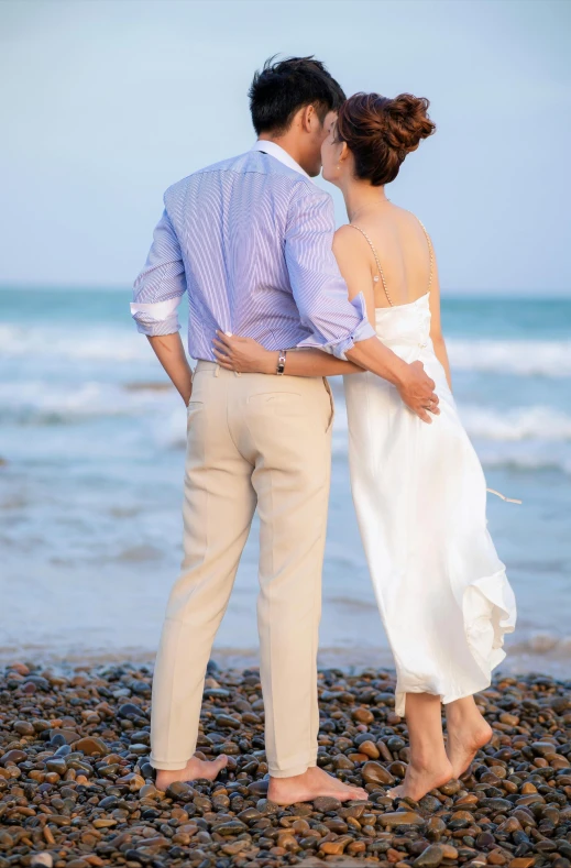 a bride and groom at the beach looking out to sea