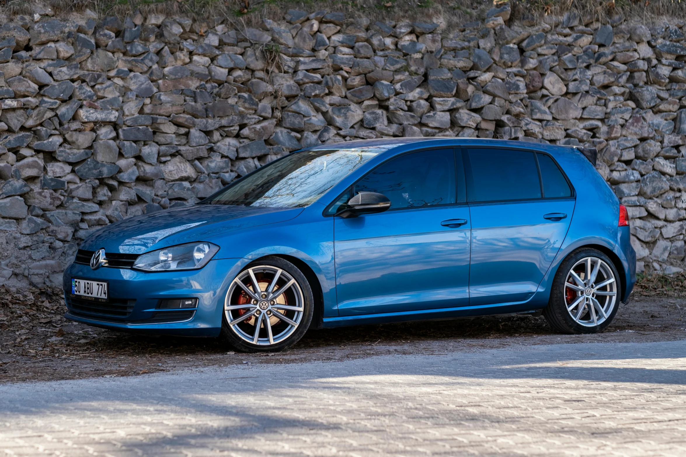 a blue volkswagen golf, on display outside a stone wall