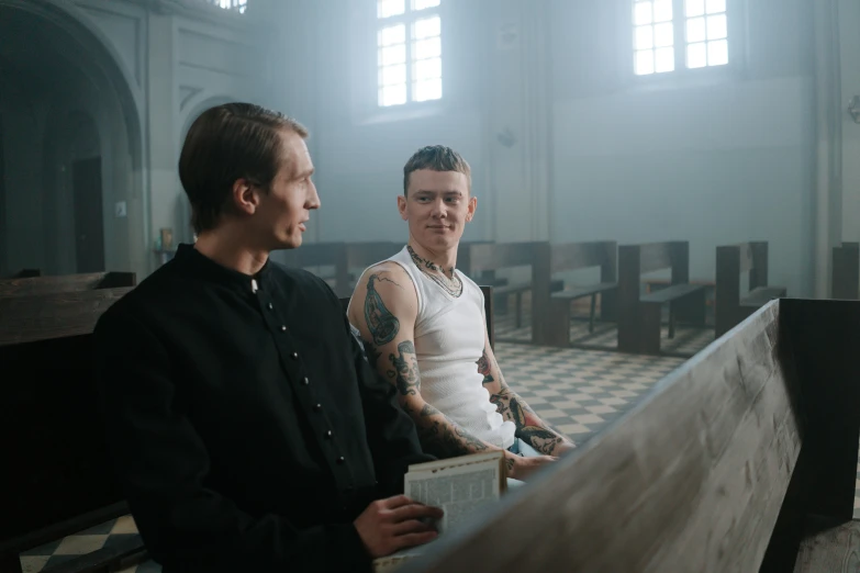 two men sitting at a pew together with a book on the ground