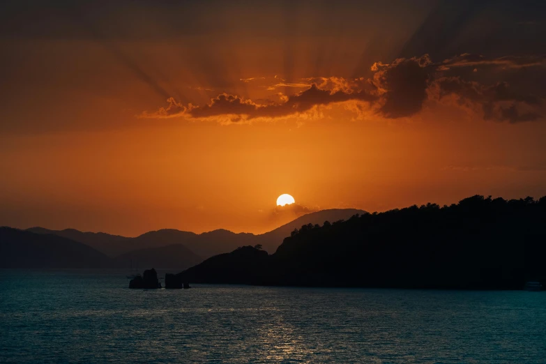 the sun rises over a mountain range overlooking a body of water