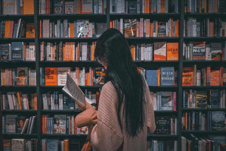 a woman looks at her book in front of an extensive bookshelf