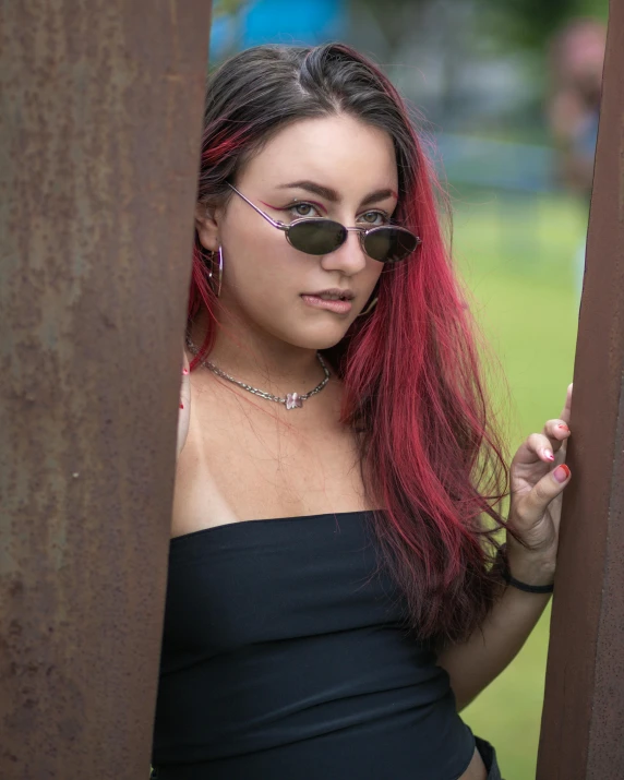 a young woman wearing sunglasses is leaning on a pole