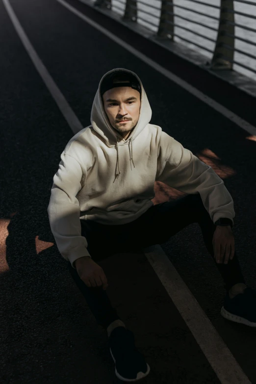 man wearing sweatshirt and black pants sitting on the street