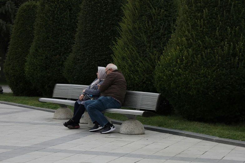 a couple sits on a park bench reading papers