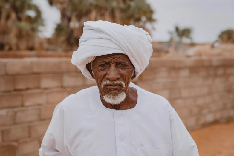 an elderly man with a turban and beard standing near brick wall