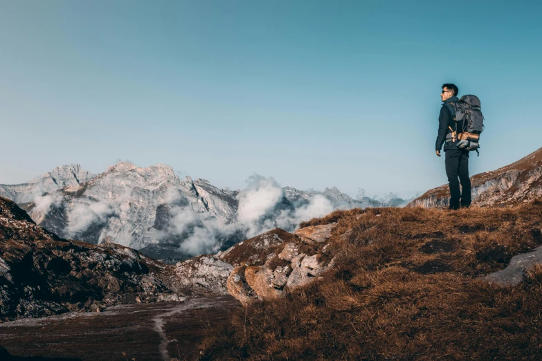 the lone hiker stands atop a ridge overlooking the mountains