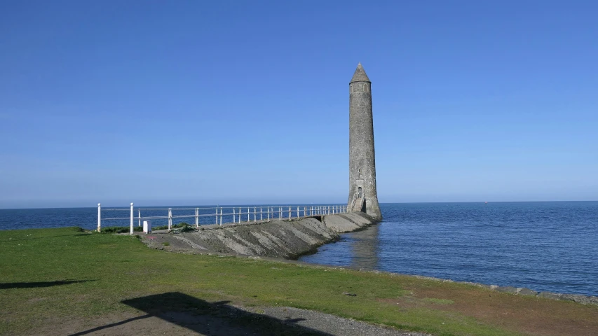 an old stone monument near the water with a long dock on one side and other end