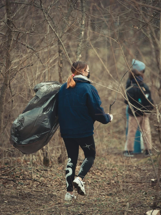 two young people walking through a forest carrying lots of stuff