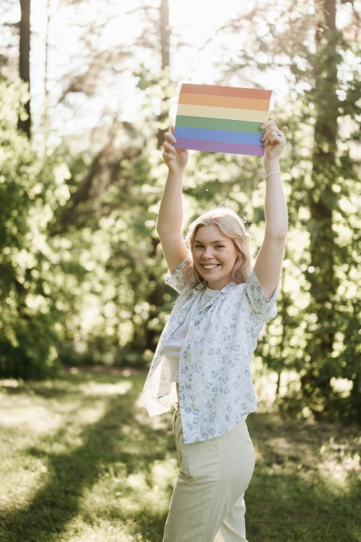 a woman holding up a rainbow flag in the forest