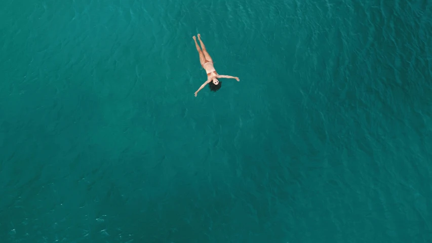 man in white swimsuit jumping off pier into blue water