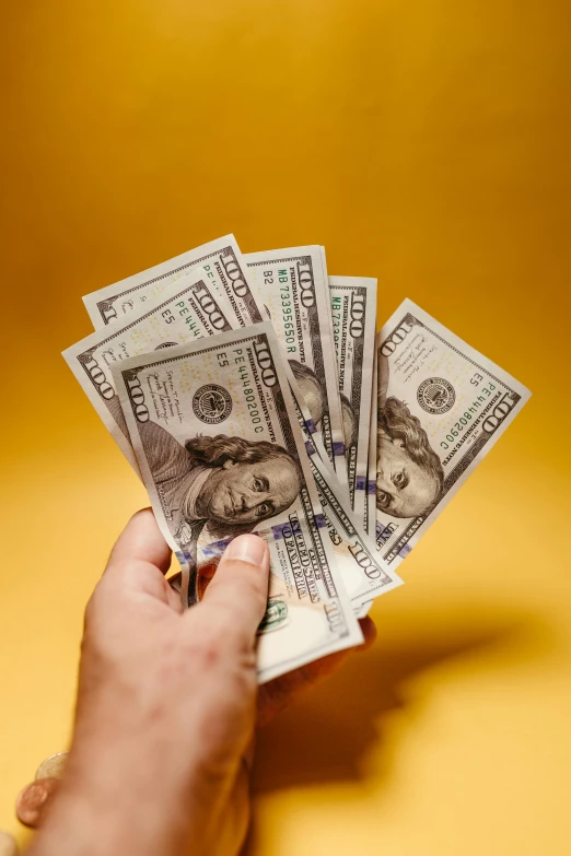 a hand holding five stacks of money on top of a table