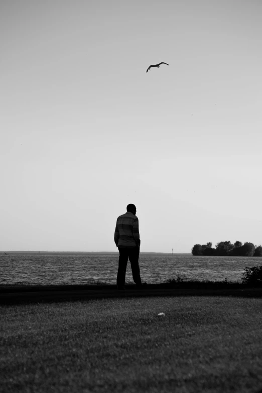 a man standing near the water flying a kite